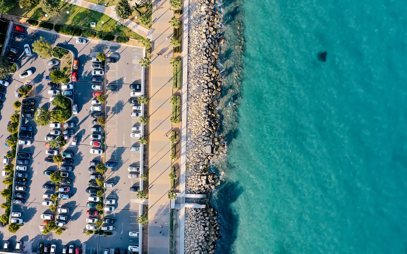 A large seafront parking lot seen from above beside clear water