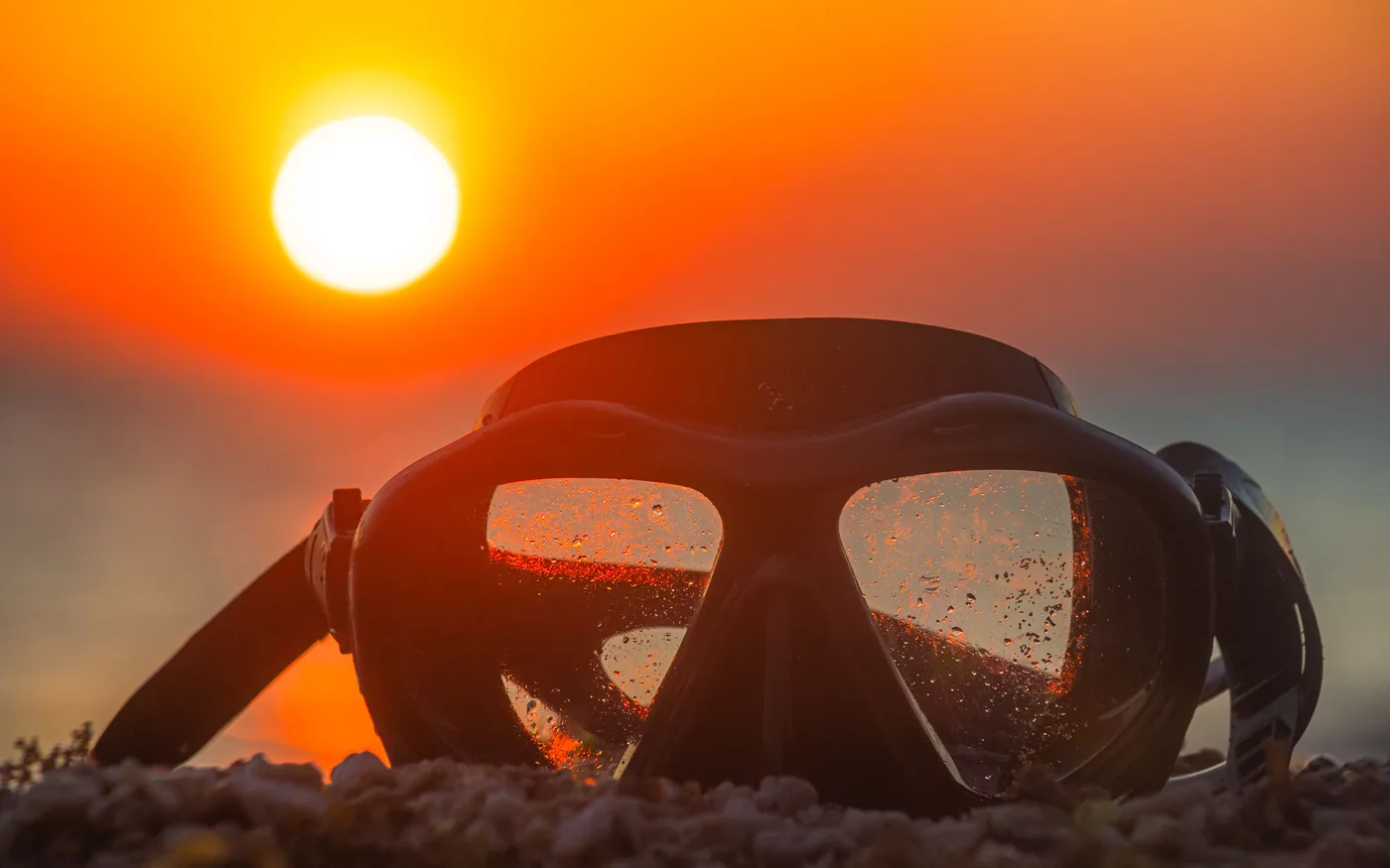 A dive mask resting on gravel against a low sun
