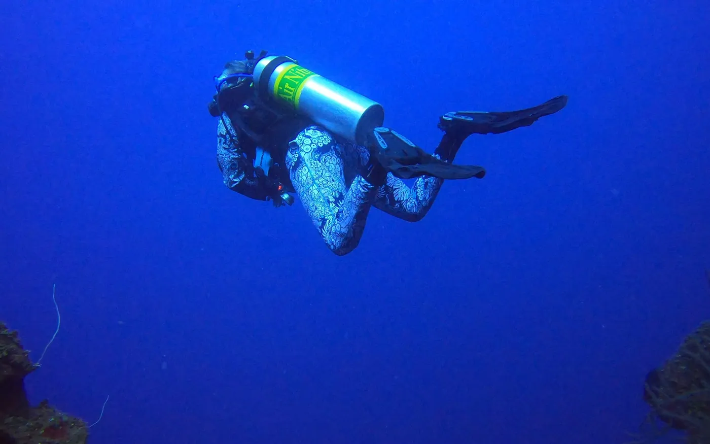 A single scuba diver in open blue water above a reef