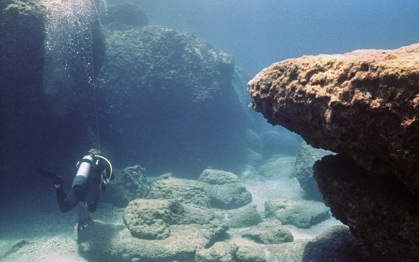 A scuba diver moving between large boulders on a rocky bottom