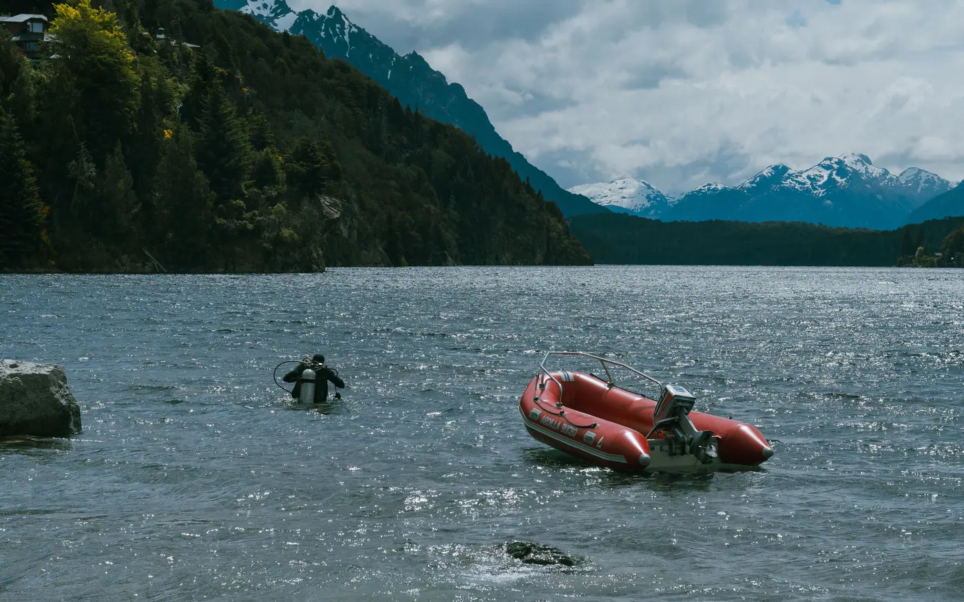 A diver in the water beside an inflatable boat in a cold mountain lake