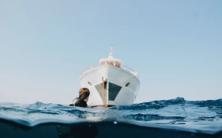 A diver in the water at the bow of a boat, half above and half below the surface