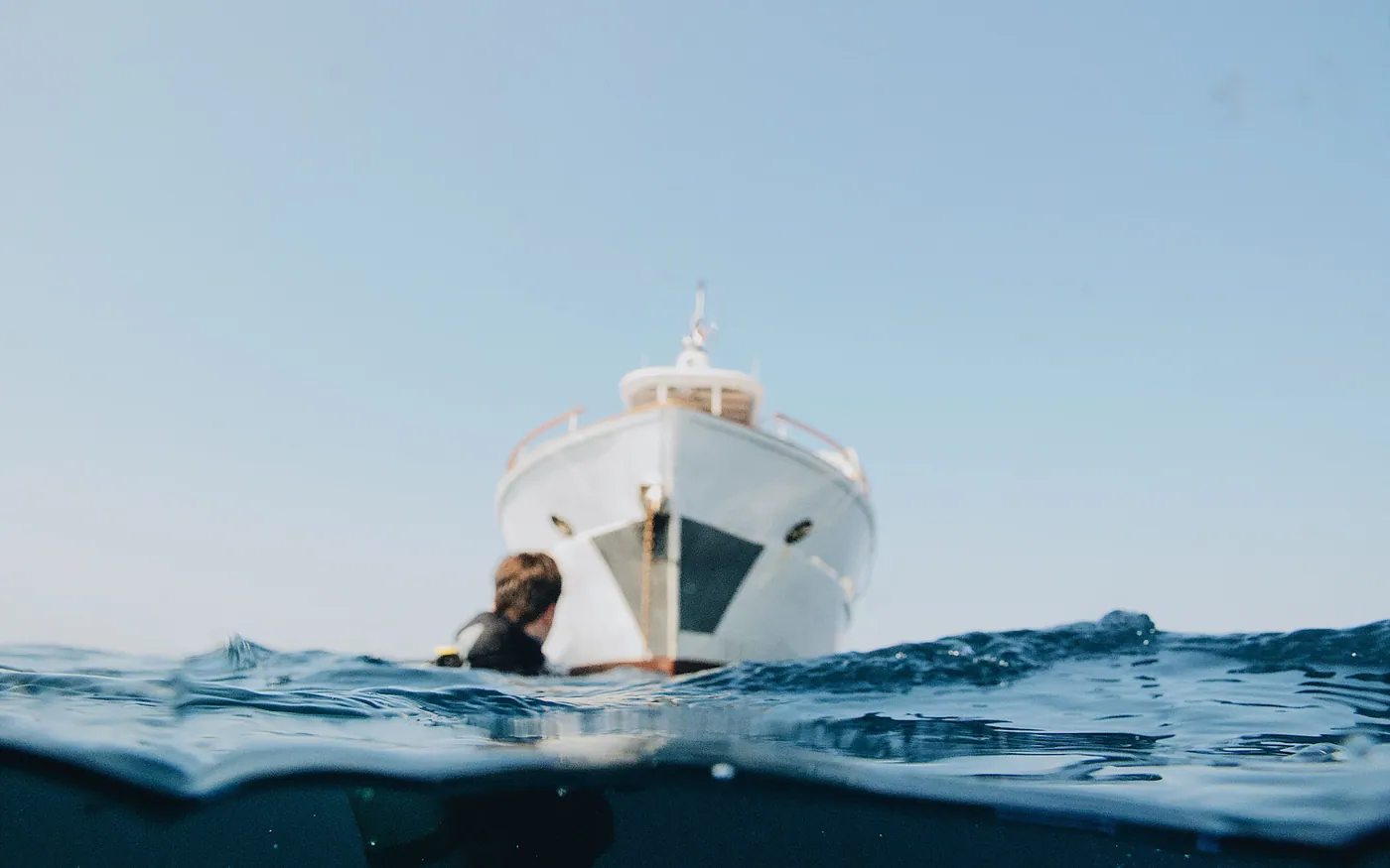 A diver in the water at the bow of a boat, half above and half below the surface