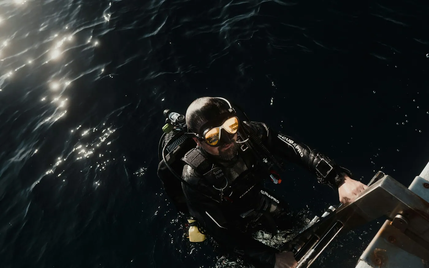 A scuba diver at the surface holding a boat ladder in dark water