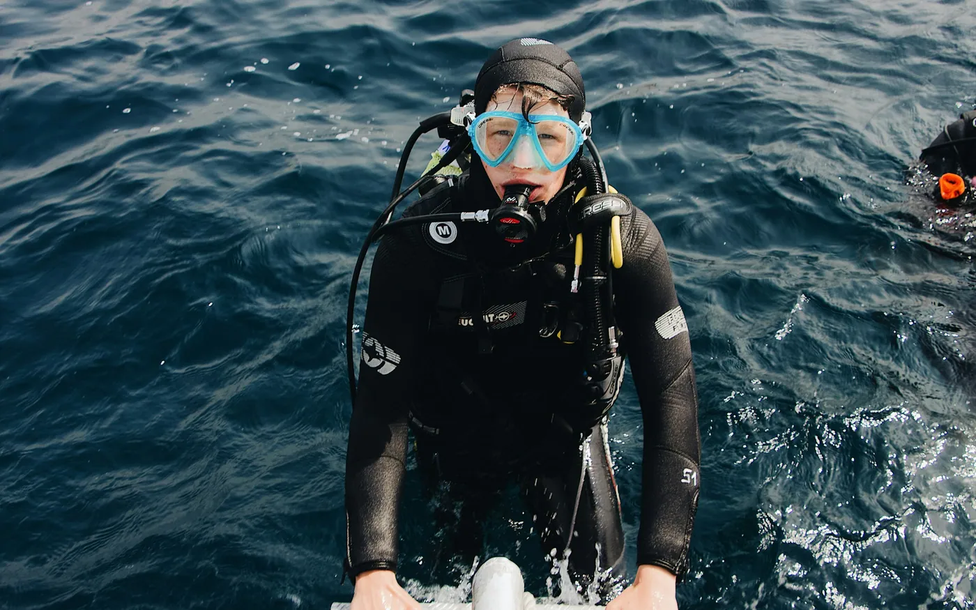 A diver in full equipment at the surface holding on beside choppy water