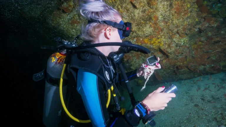 A scuba diver checking an instrument on the wrist while holding a light