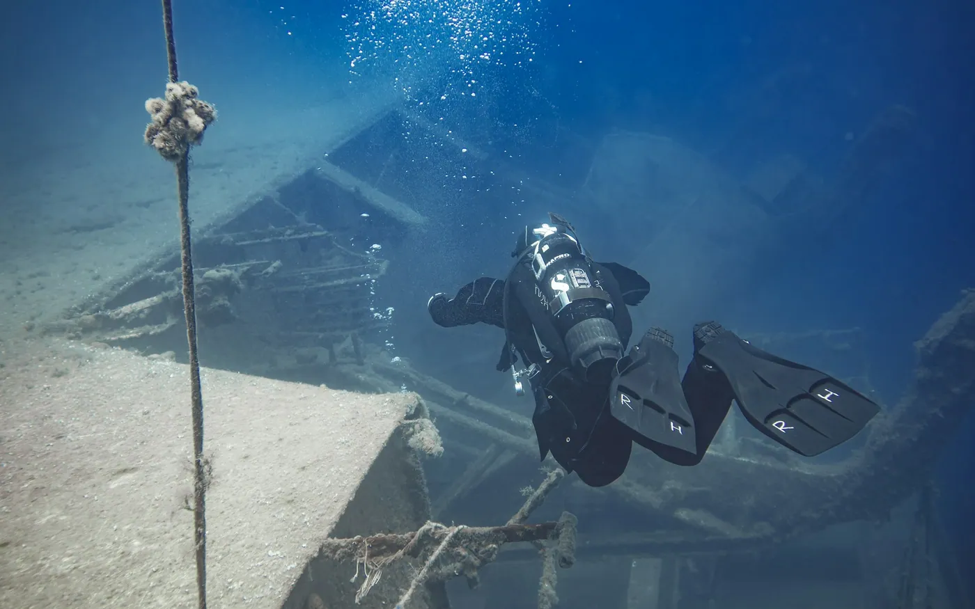 A scuba diver descending beside a shot line towards a wreck