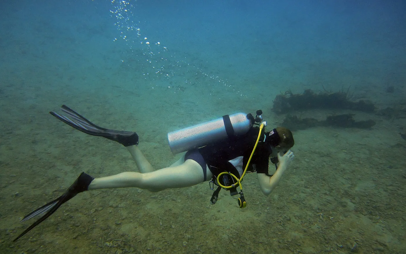 A scuba diver swimming slowly along a sandy bottom