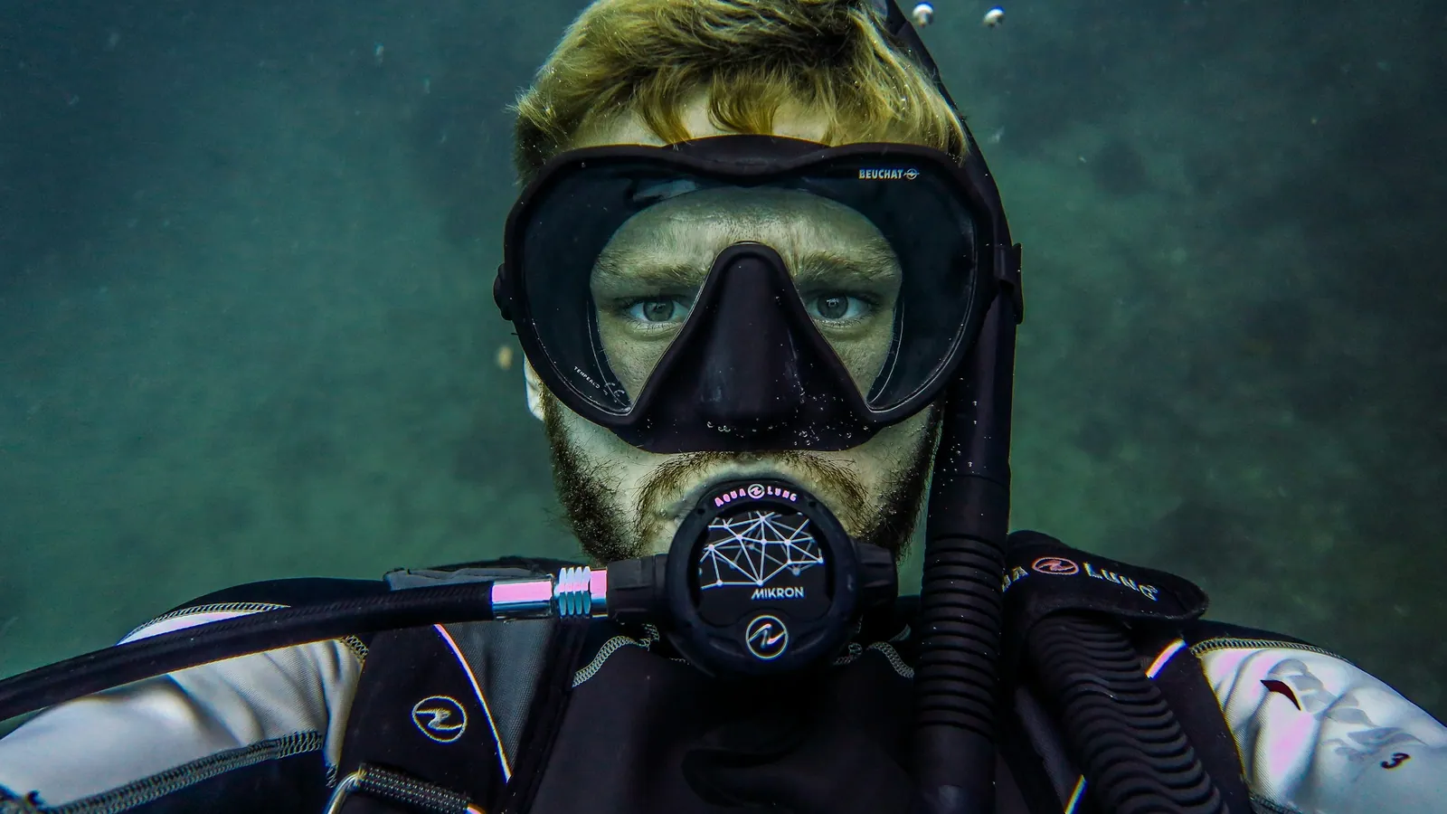 A diver in a hooded dry suit at the surface with the regulator in