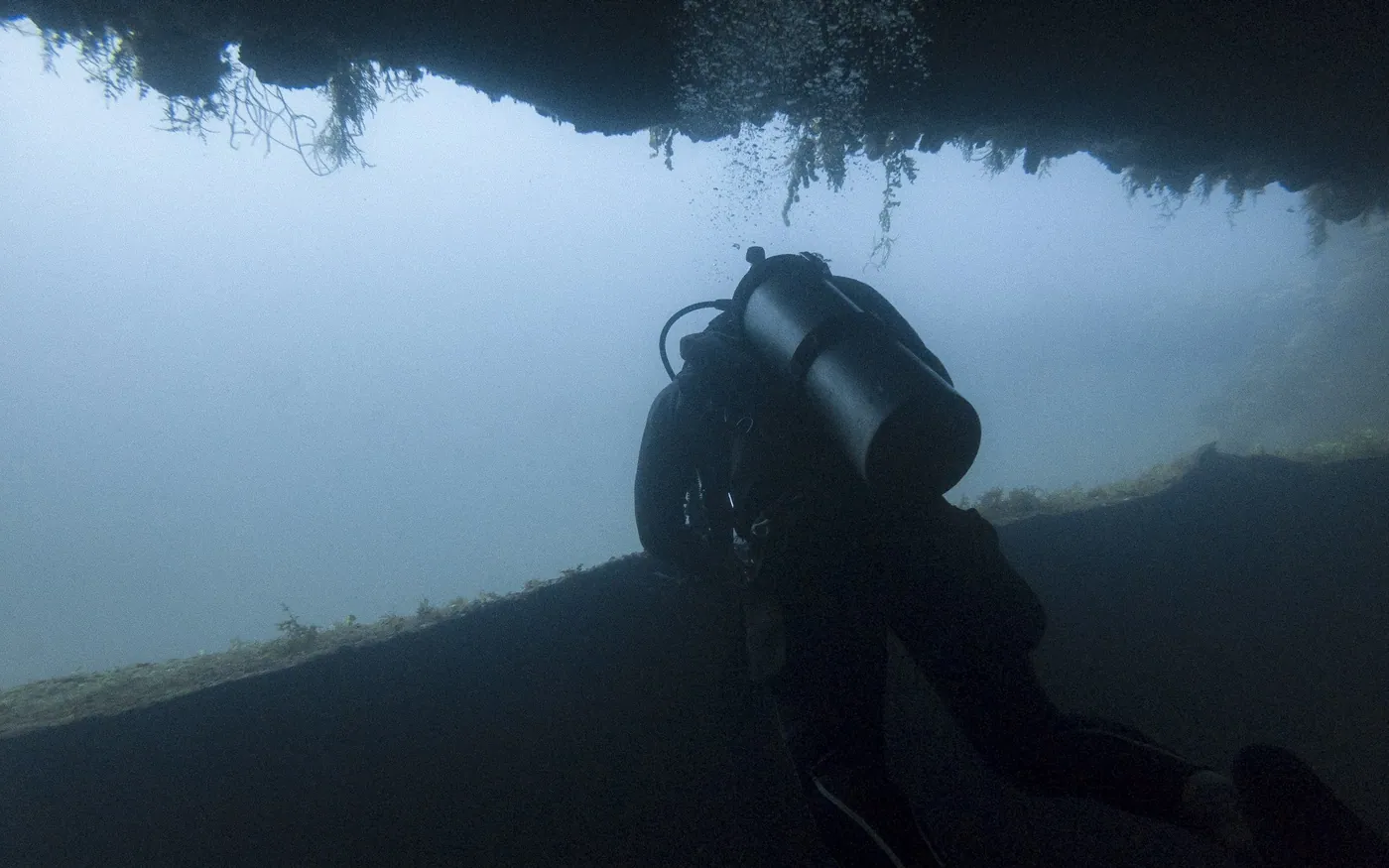 A scuba diver under a structure in dim green water