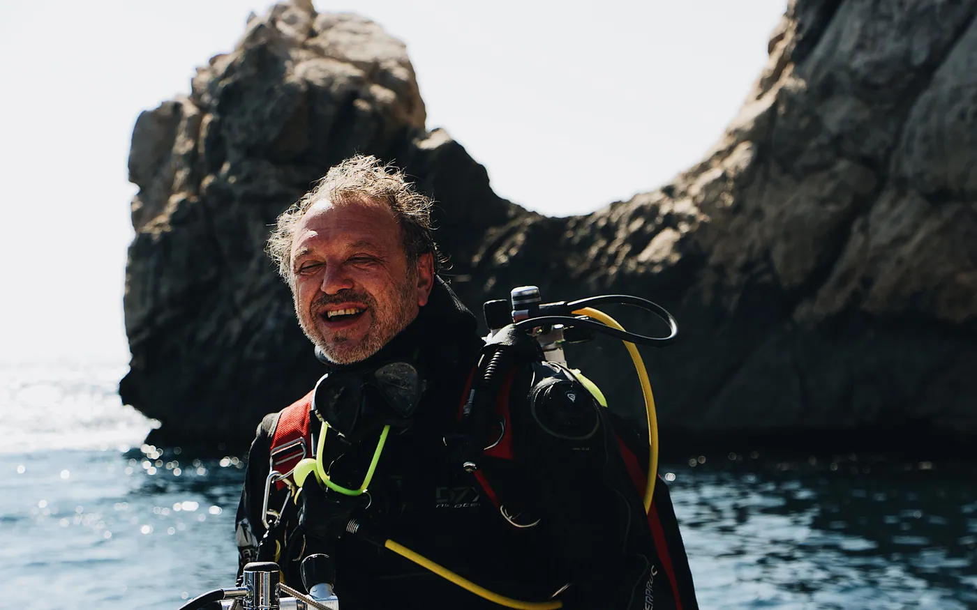 A scuba diver in full equipment standing in the water below a rock arch