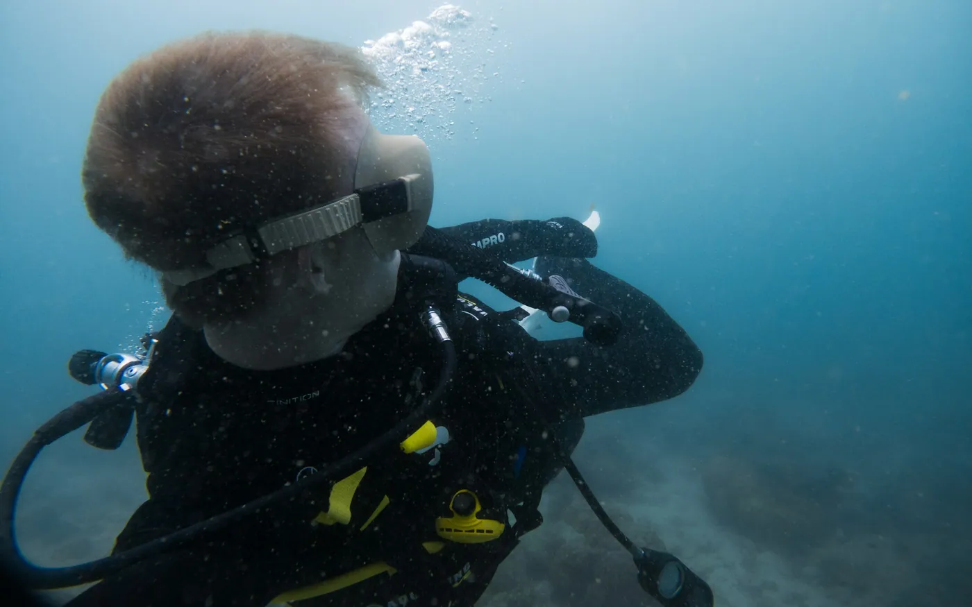 A scuba diver in green coastal water with the regulator in