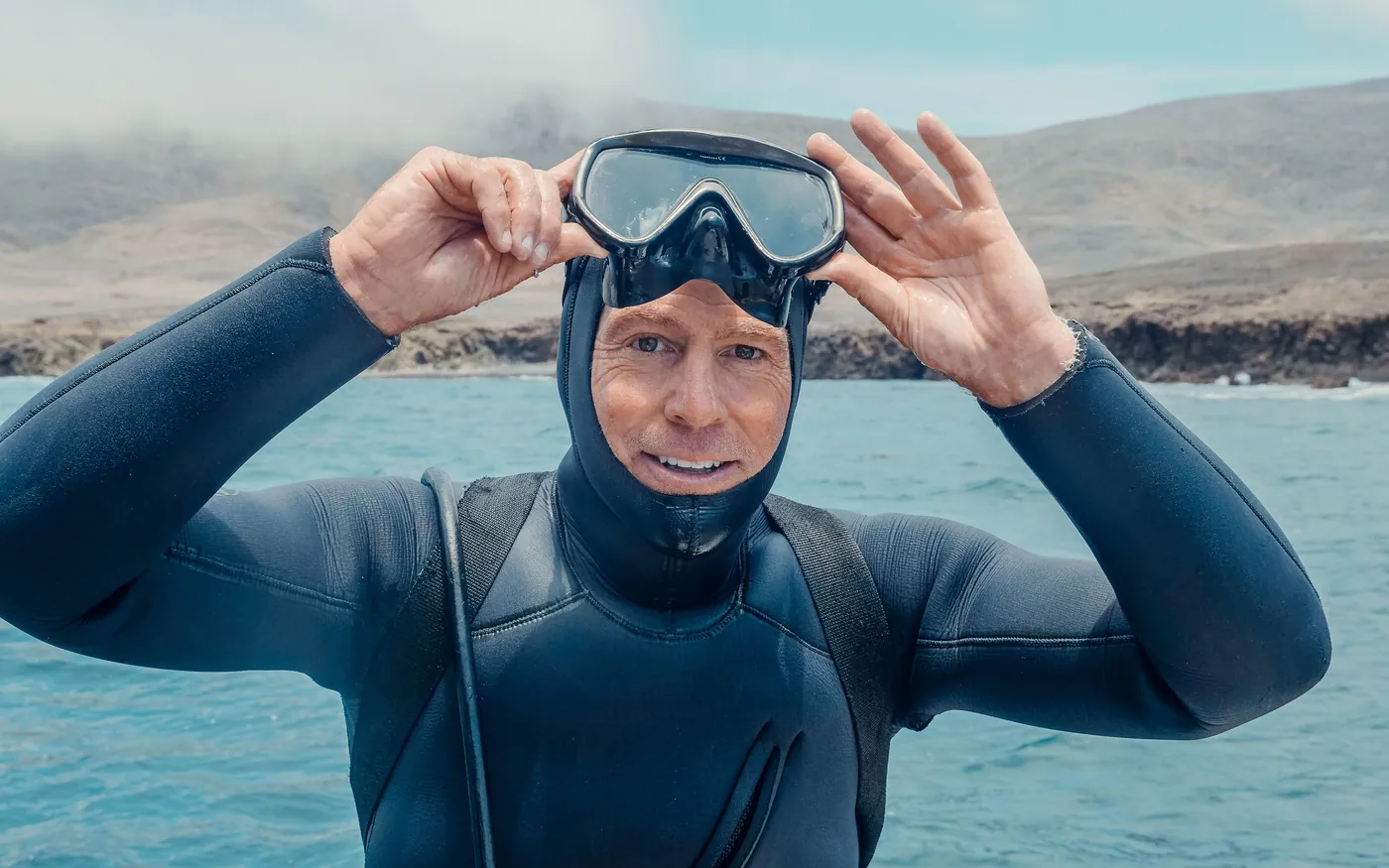 A diver in a hooded wetsuit lifting a mask up onto the forehead