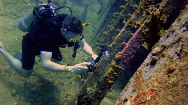 A scuba diver photographing the encrusted structure of a wreck
