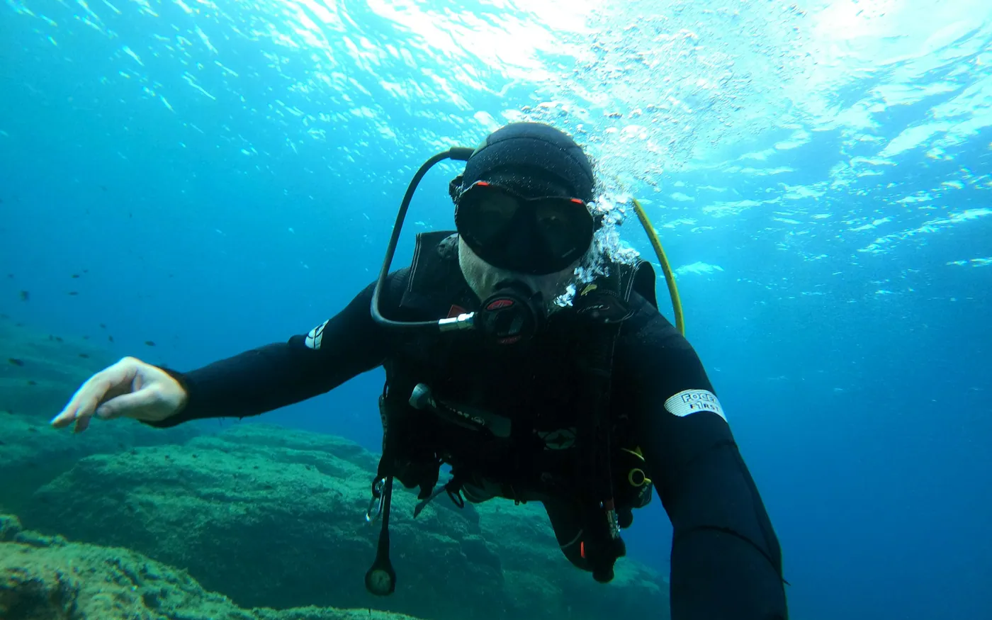 A scuba diver reaching forward in green water near the surface