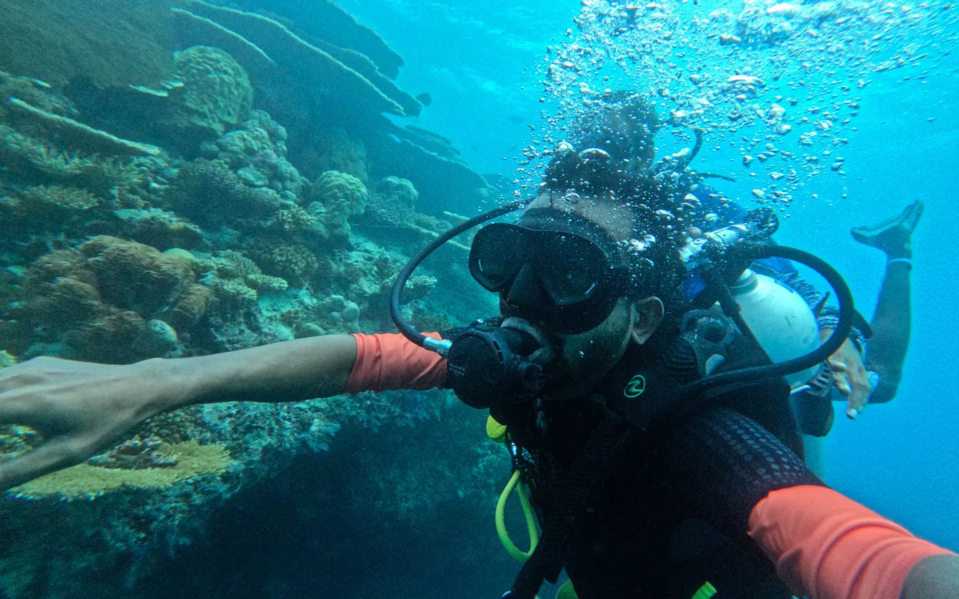 A scuba diver reaching forward over a shallow reef