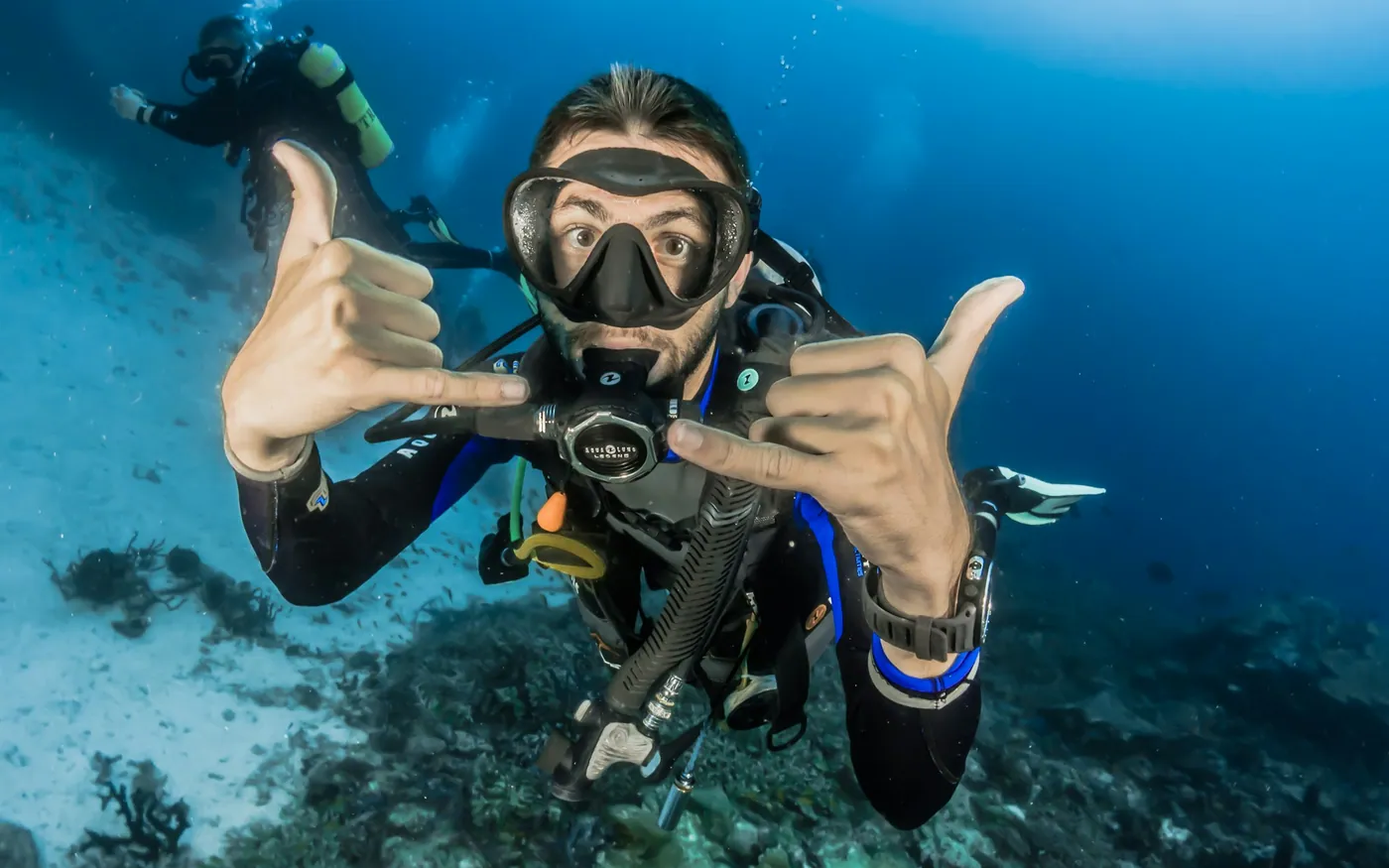 A scuba diver in full equipment signalling cheerfully above a reef