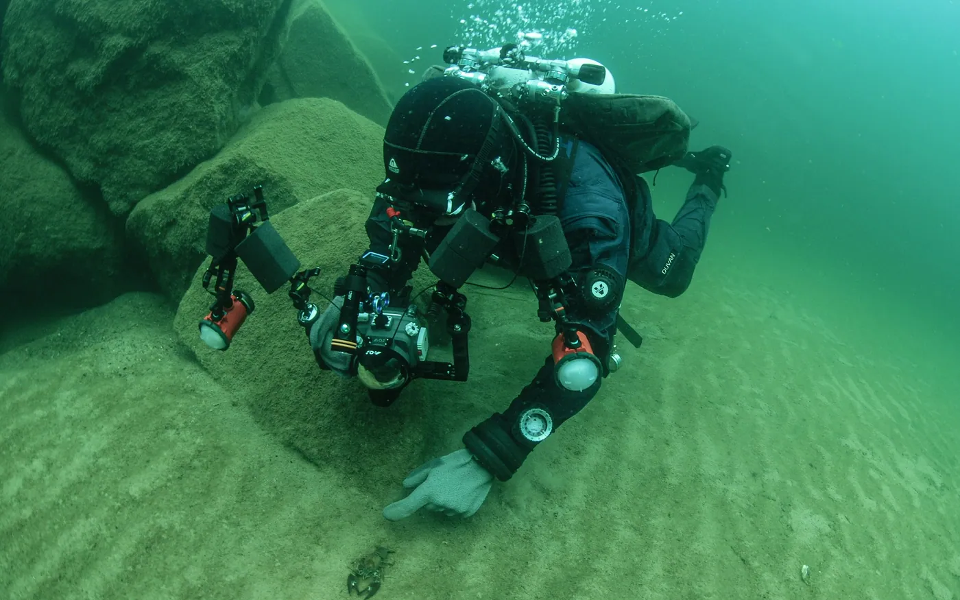 A scuba diver settling a large camera rig on a sandy bottom