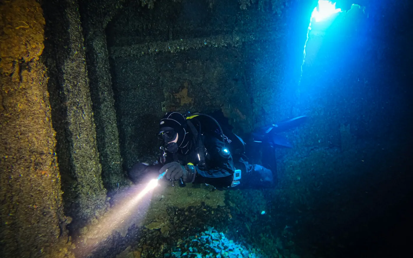 A scuba diver shining a light along the inside of a wreck