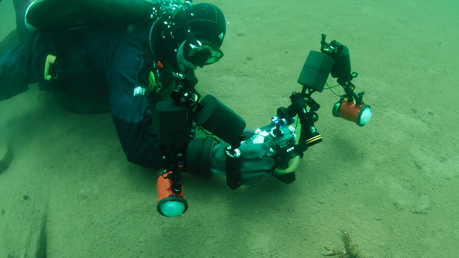 A scuba diver settling a large camera and lighting rig on a sandy bottom