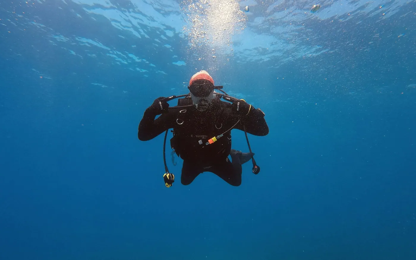 A diver in a dry suit descending through blue water