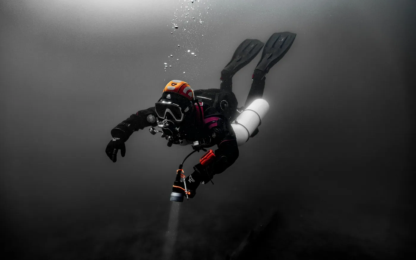 A diver in a dry suit carrying a light in dark water
