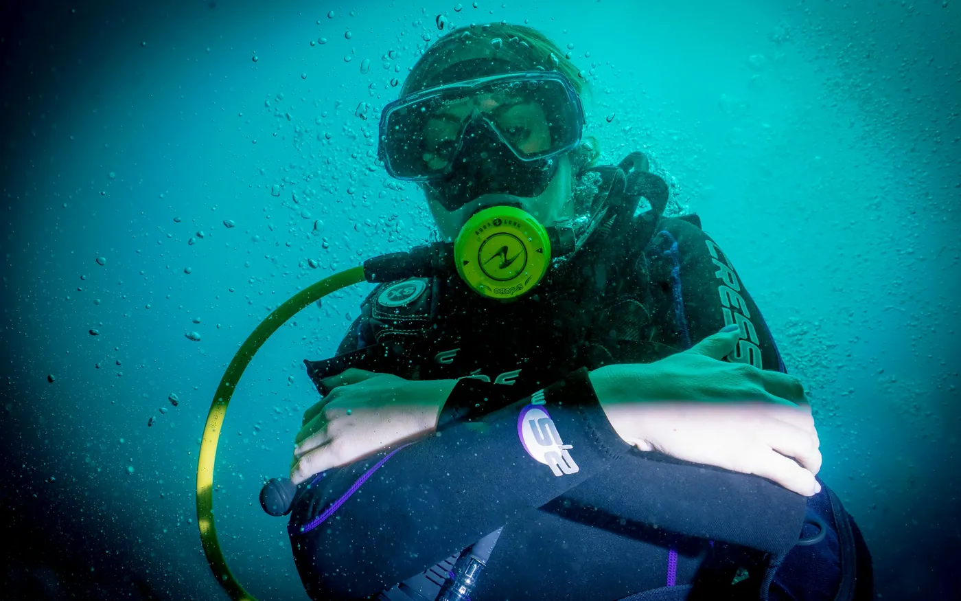 A diver underwater in a dry suit with the inflator valve on the chest