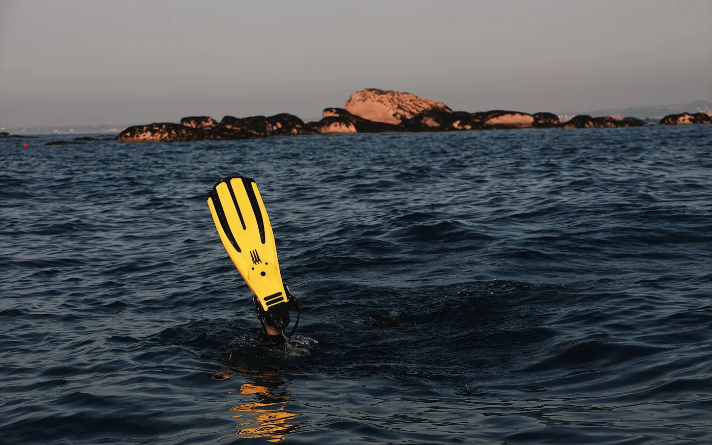 A yellow dive fin held clear of the surface in grey water