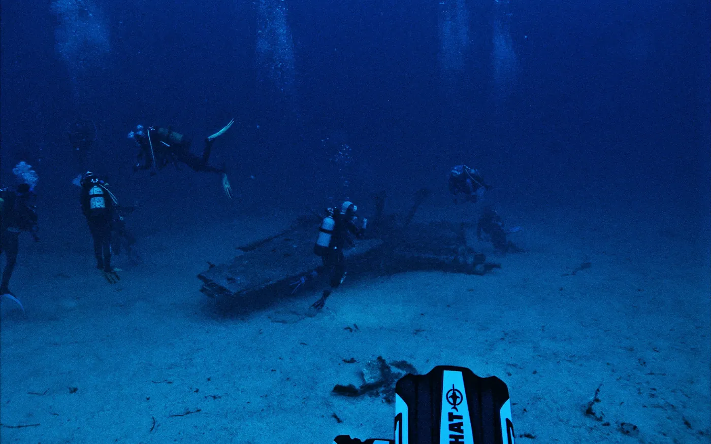Several scuba divers spread out above a debris field in deep water