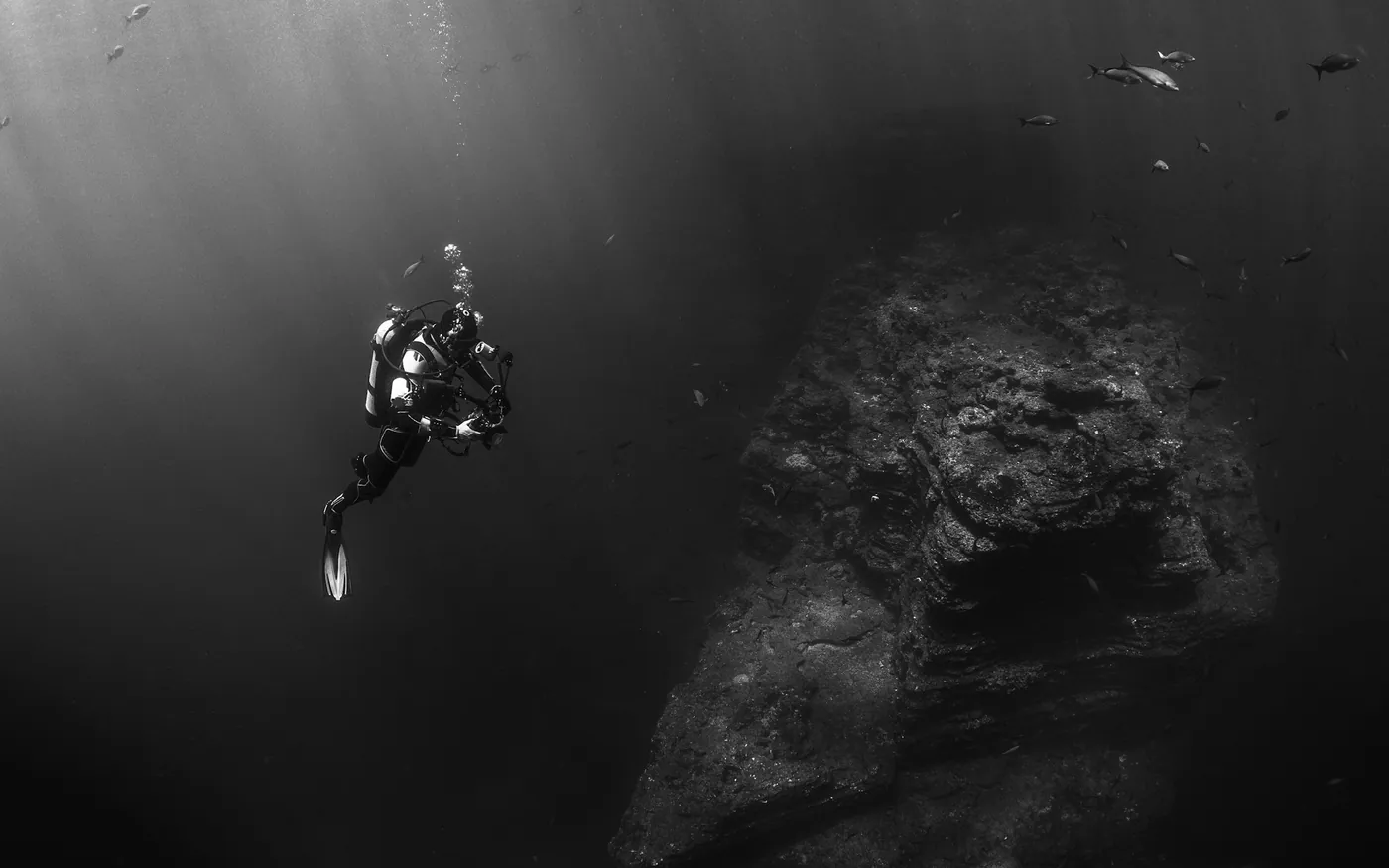 A lone scuba diver in black and white above a large rock