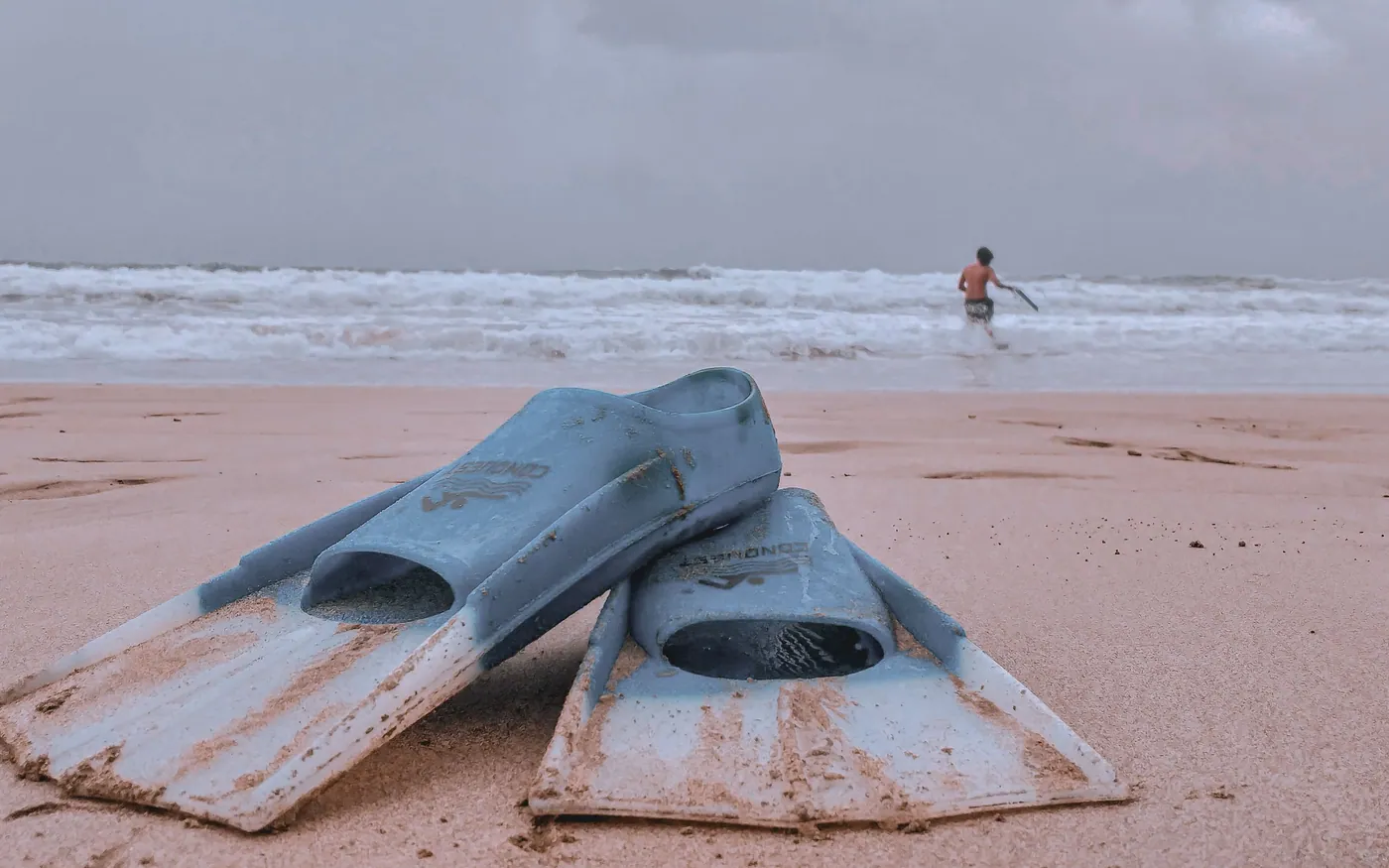 A pair of dive fins resting on a beach with the sea behind