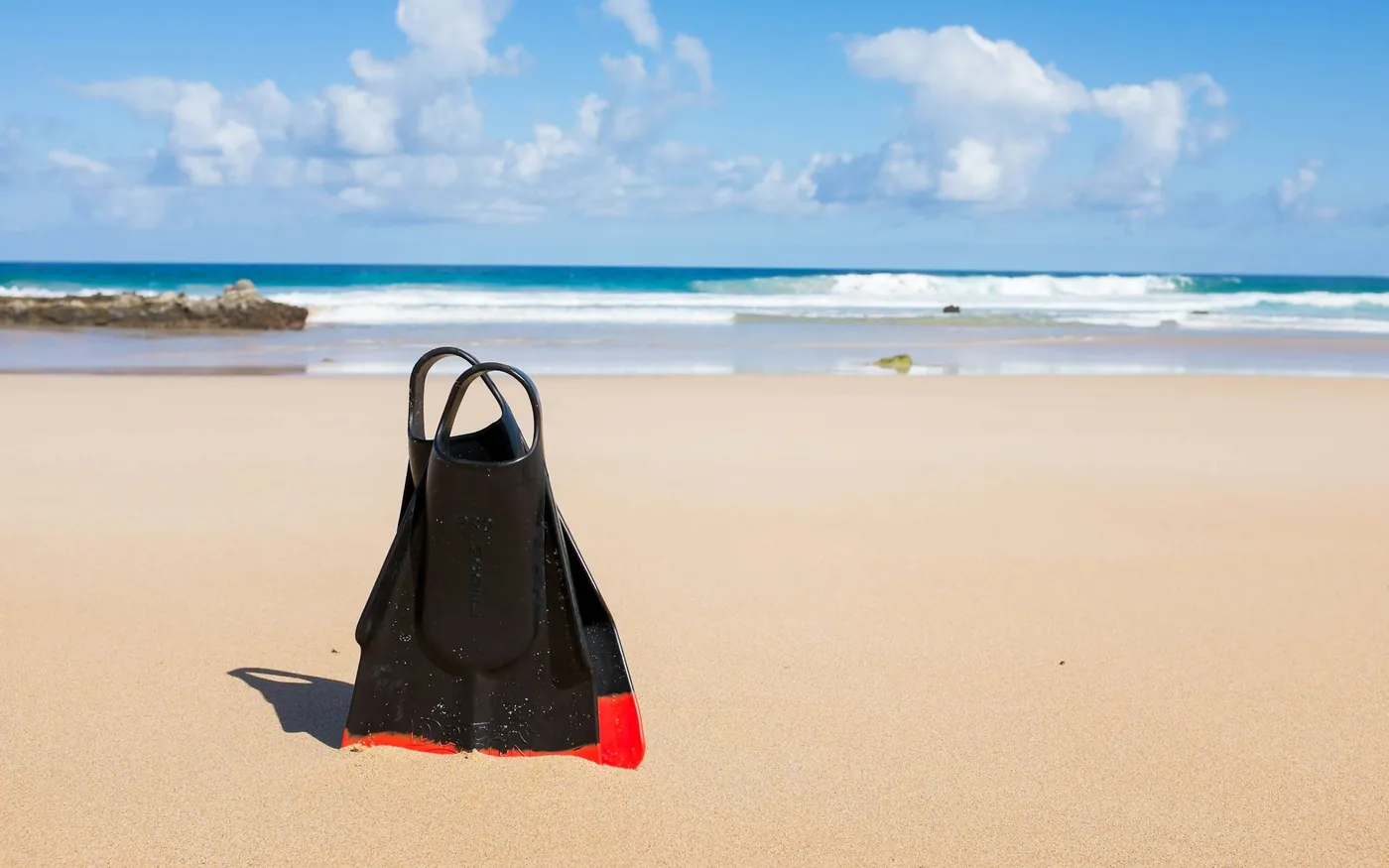 A pair of dive fins standing upright on a sandy beach