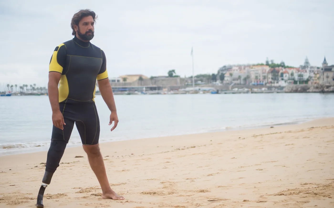 A person in a short-sleeved wetsuit walking along a beach on a warm day