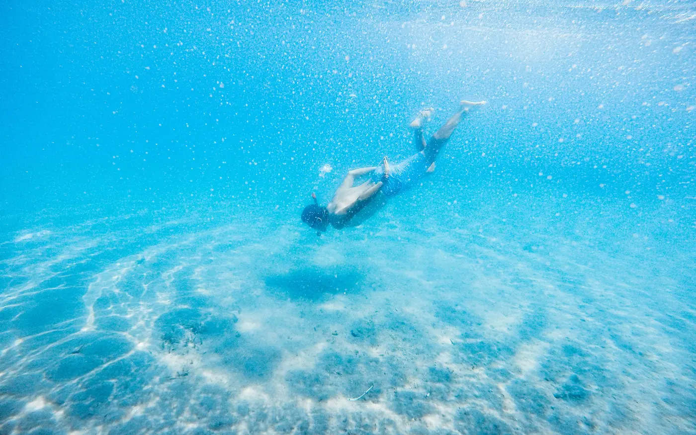 A snorkeler moving over rippled sand in clear shallow water