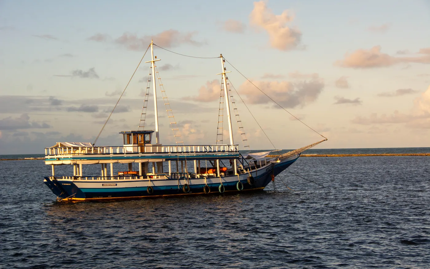A wooden two-masted boat at anchor at sunset
