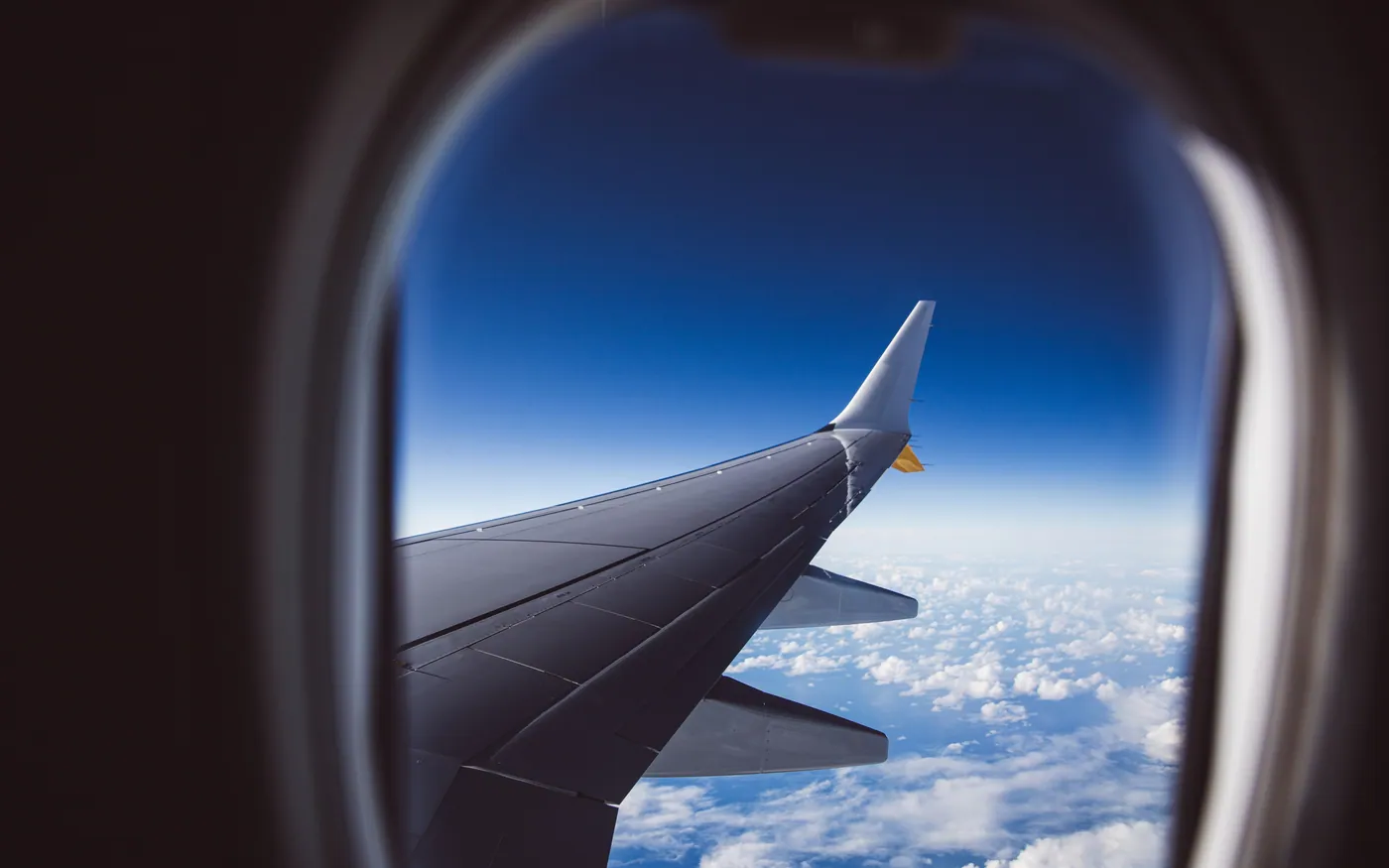 An aircraft wing seen through a cabin window above the clouds