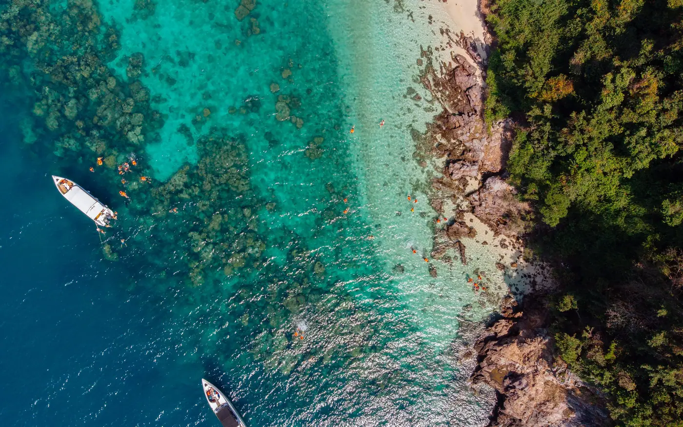 Two boats anchored off a beach beside a shallow reef