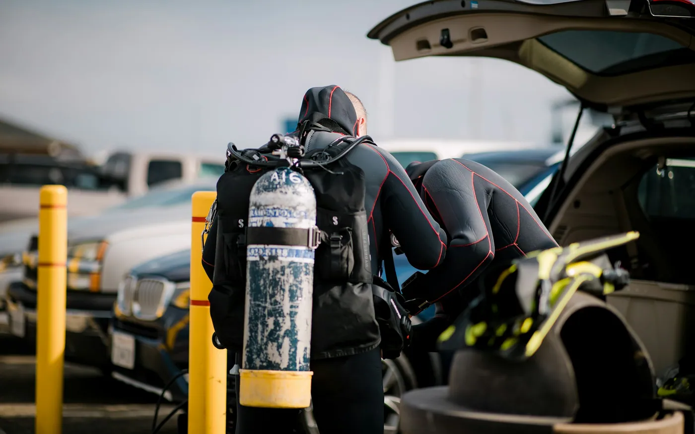 A diver in a wetsuit loading a scuba cylinder and BCD into a car