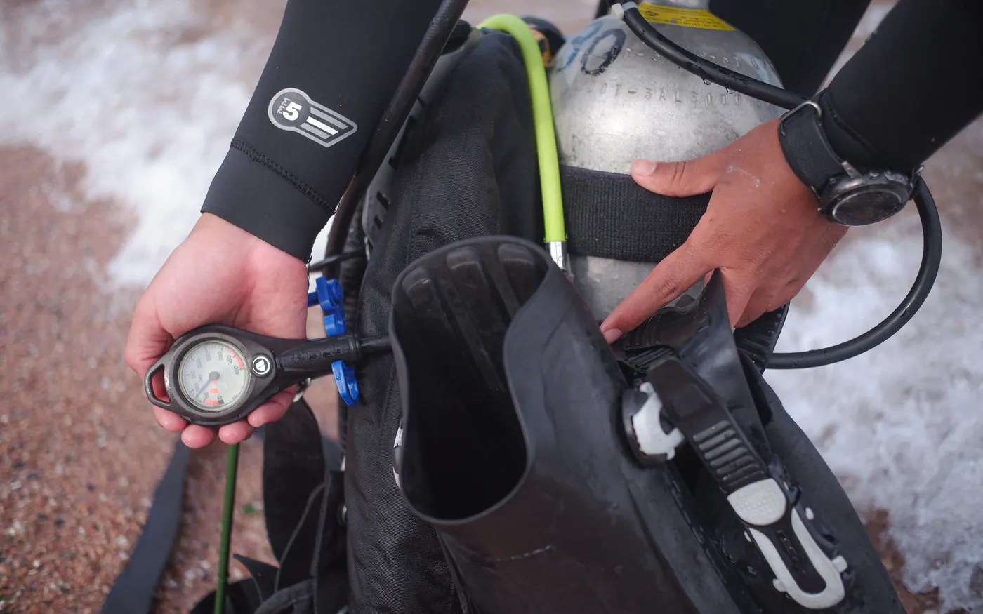 A diver checking the pressure gauge and inflator hose on a BCD before a dive