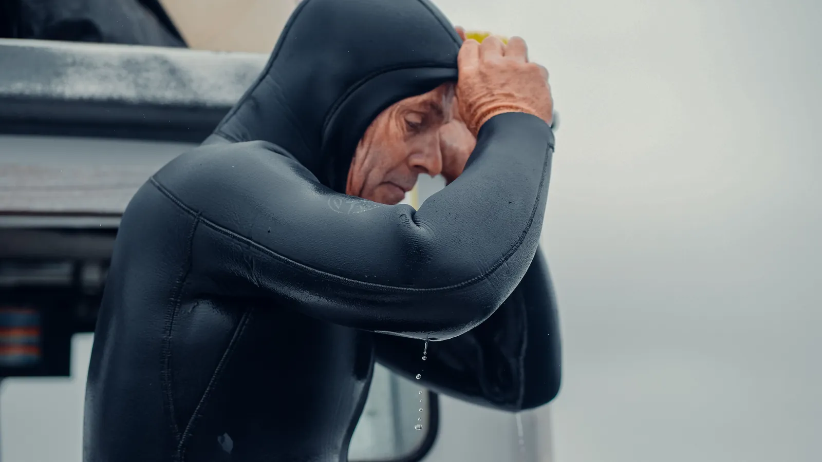 A diver in a hooded wetsuit resting against a boat rail after a cold dive
