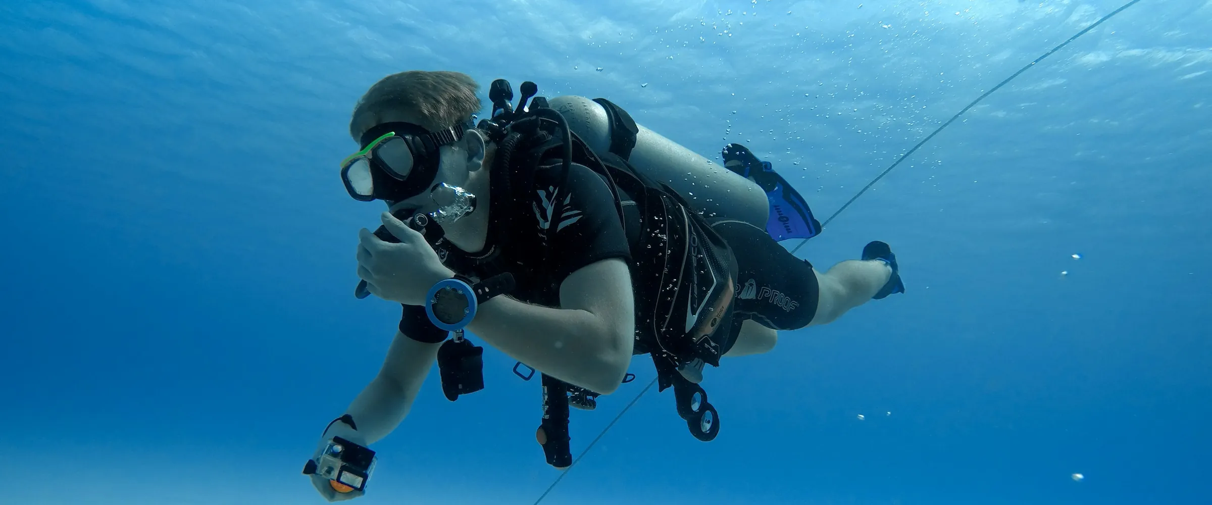 A scuba diver in full gear swimming in clear blue water a few feet down