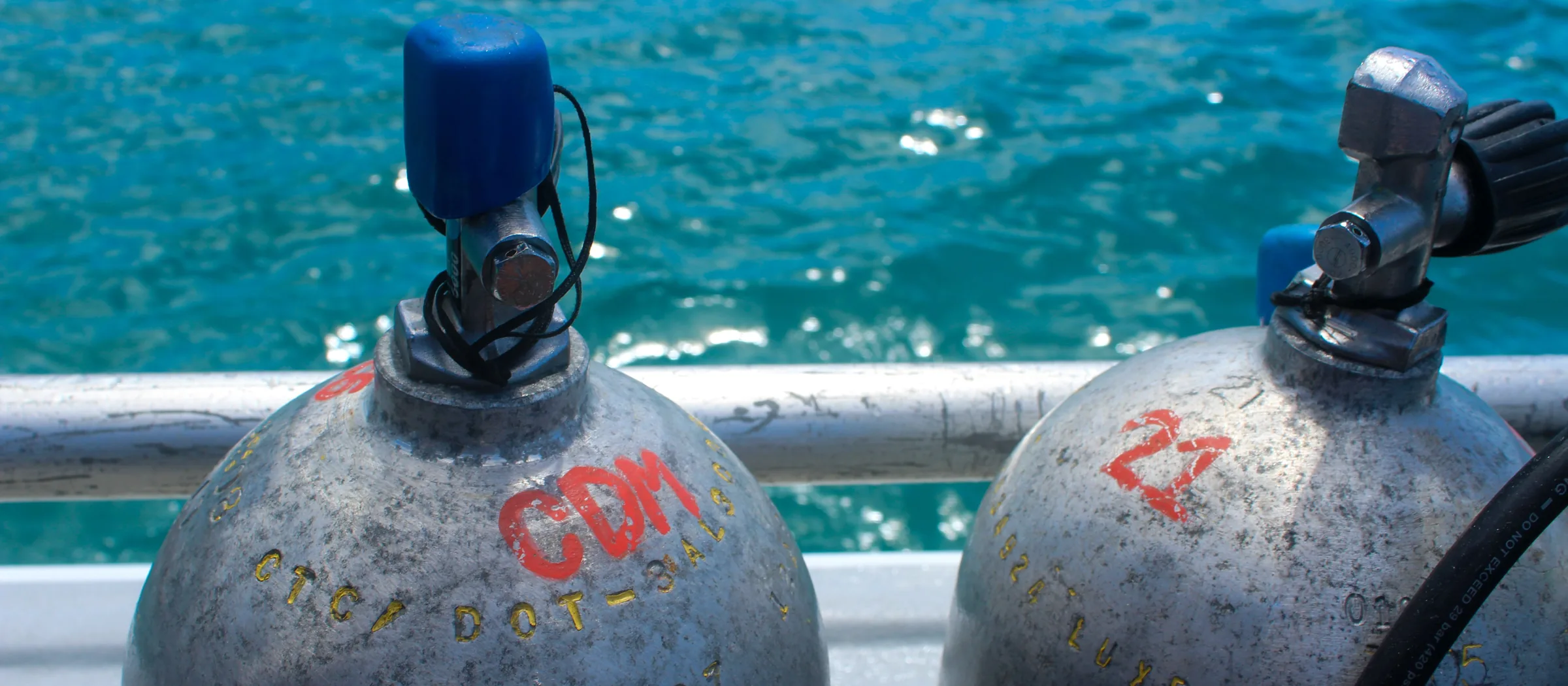 The crowns and valves of two scuba cylinders standing on a boat rail, with the sea behind
