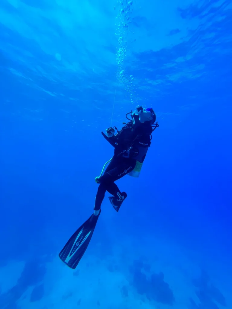 A scuba diver in full gear descending into clear deep blue water