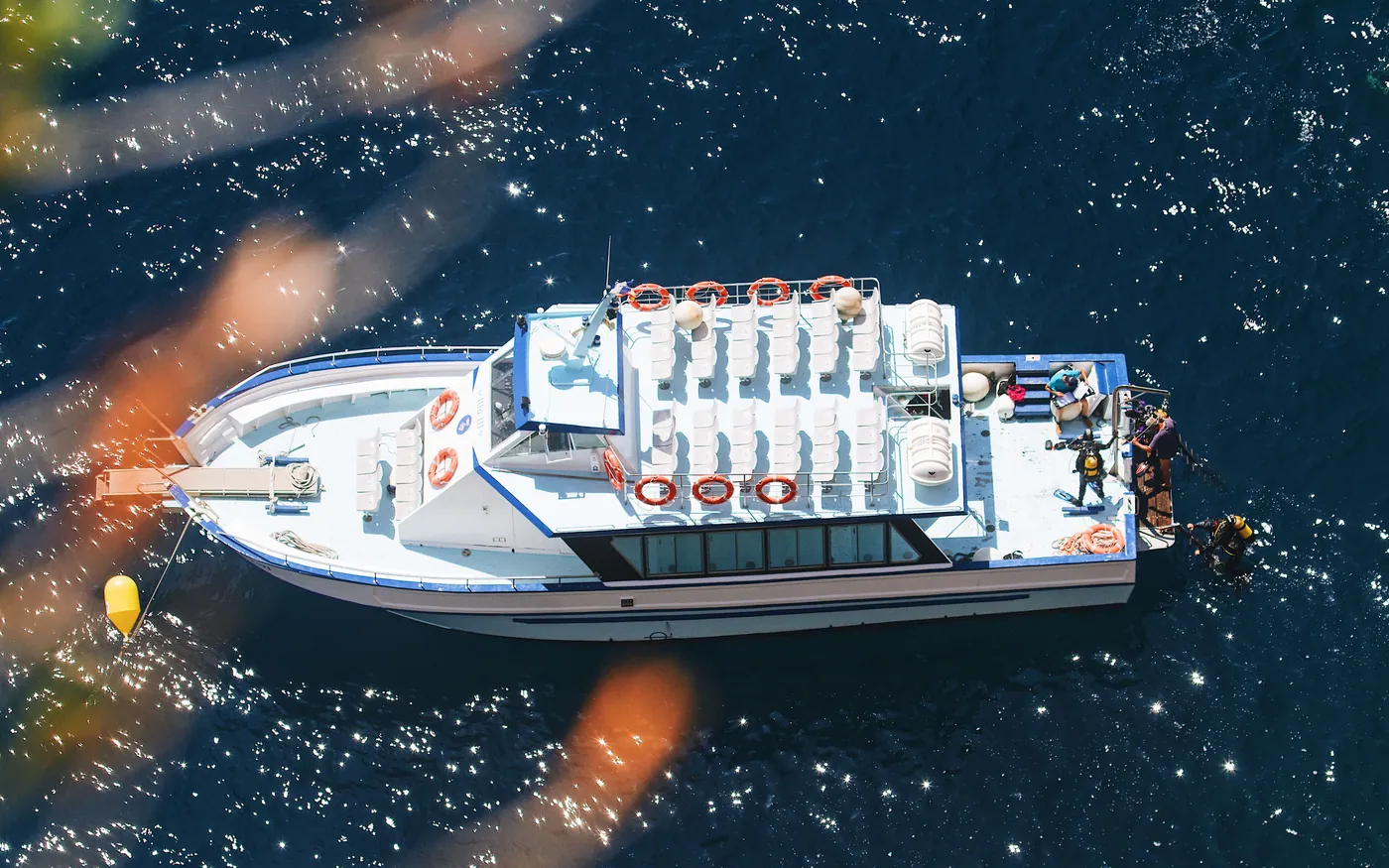 A dive boat photographed from above with divers in the water alongside
