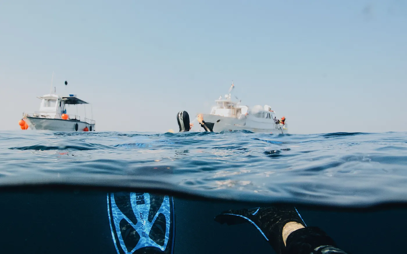 A split-level view of dive boats on the surface with a diver's fins below