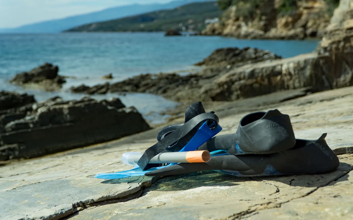 A dive mask, fins and snorkel laid out on rocks beside the sea