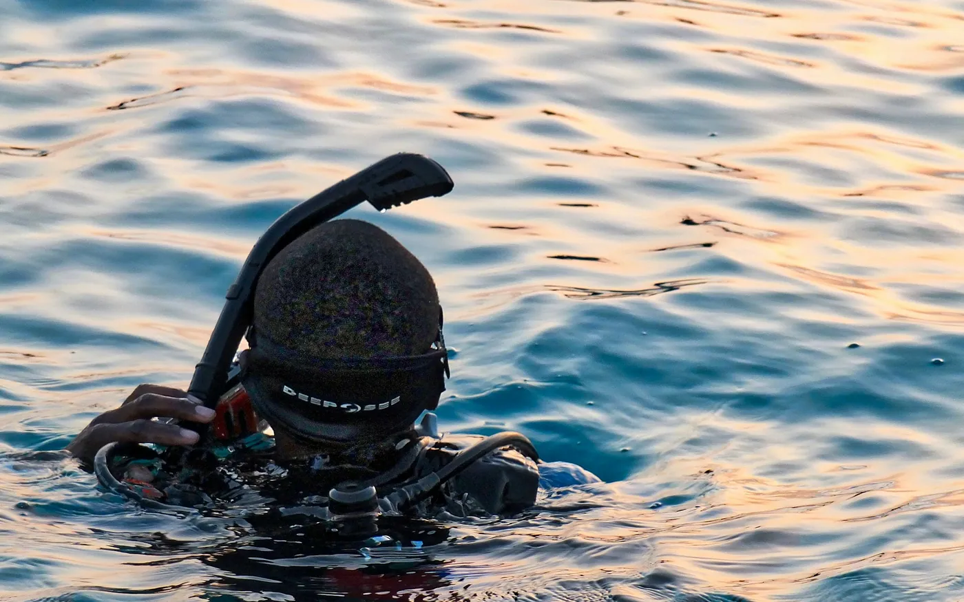 A diver adjusting a hood and snorkel at the surface at dusk