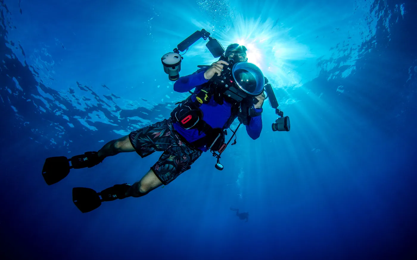 A scuba diver in full gear against the sun near the surface