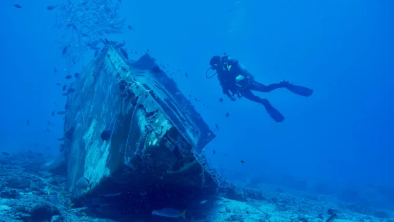 A scuba diver alongside a wreck lying in deep blue water