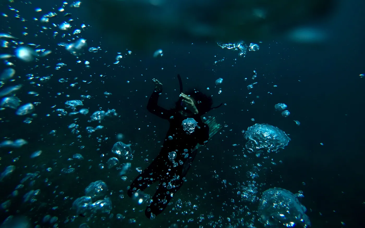 A scuba diver surrounded by rising bubbles in dark green water